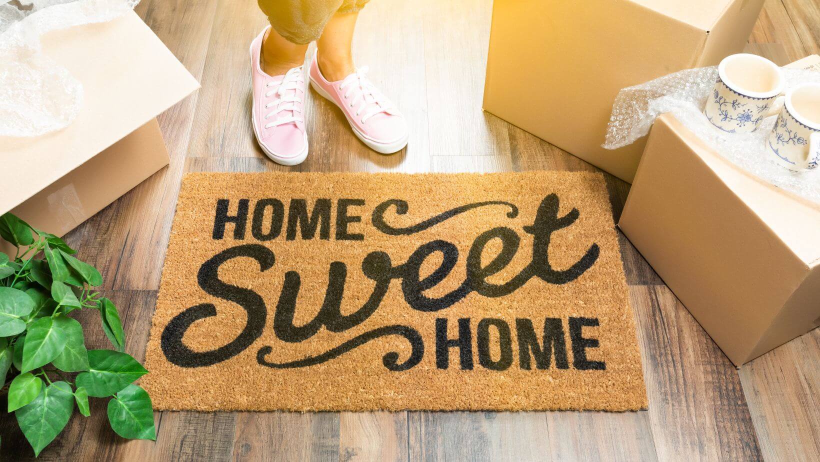 A woman standing in front of a door mat that says "Home Sweet Home"