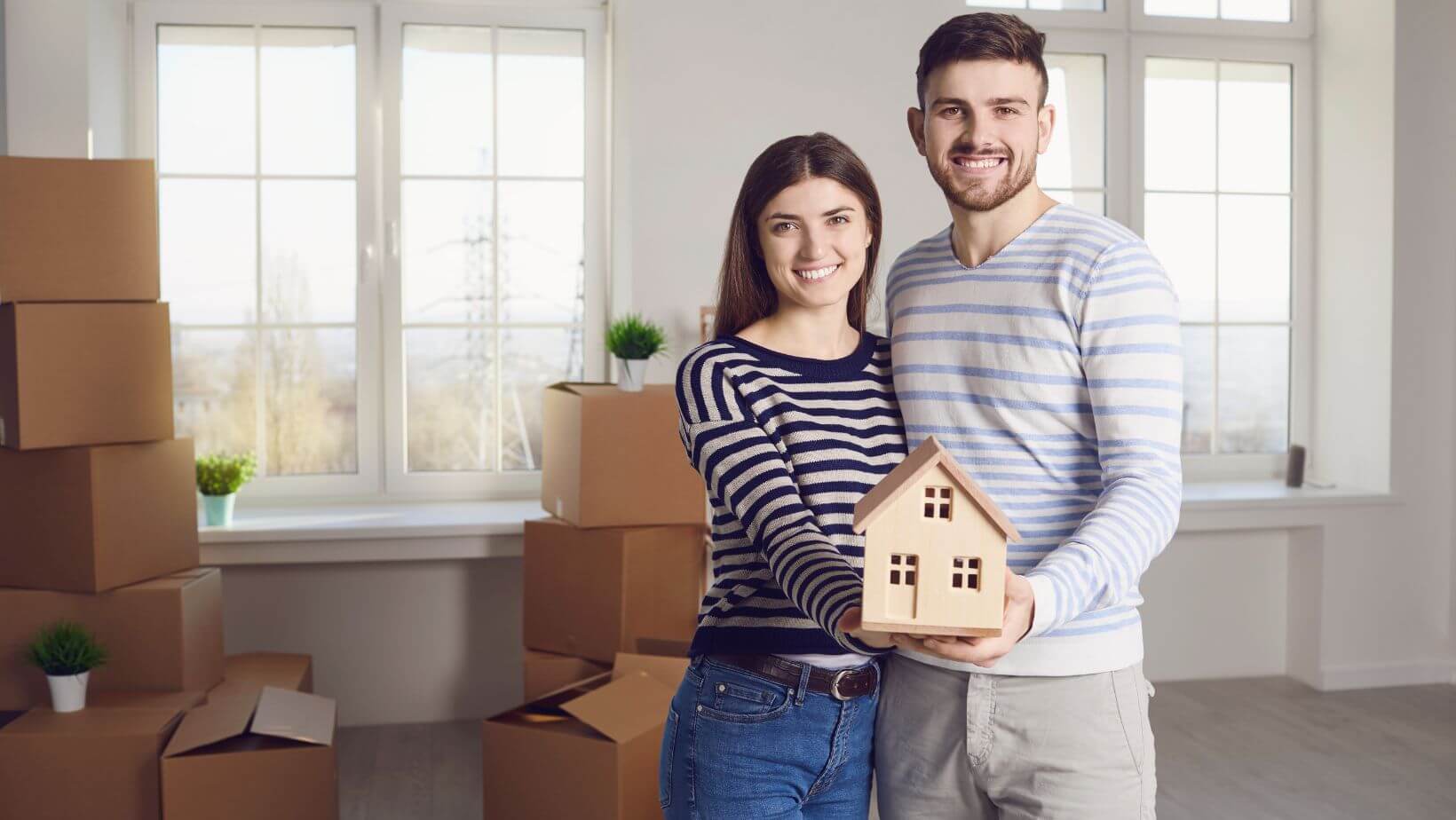 A couple in their new house holding a tiny wooden home.