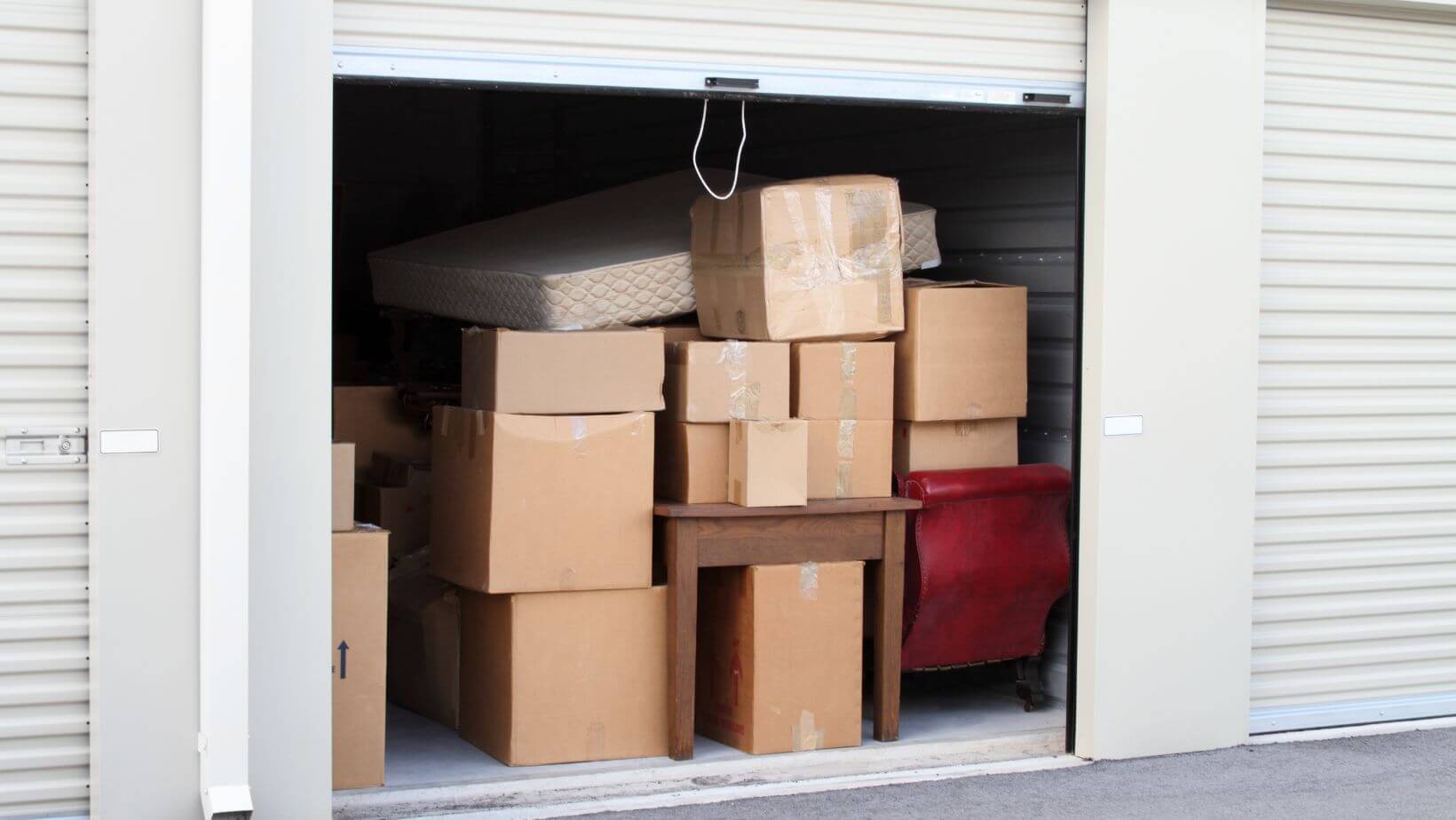 a self storage unit with the door open, boxes and furniture inside.