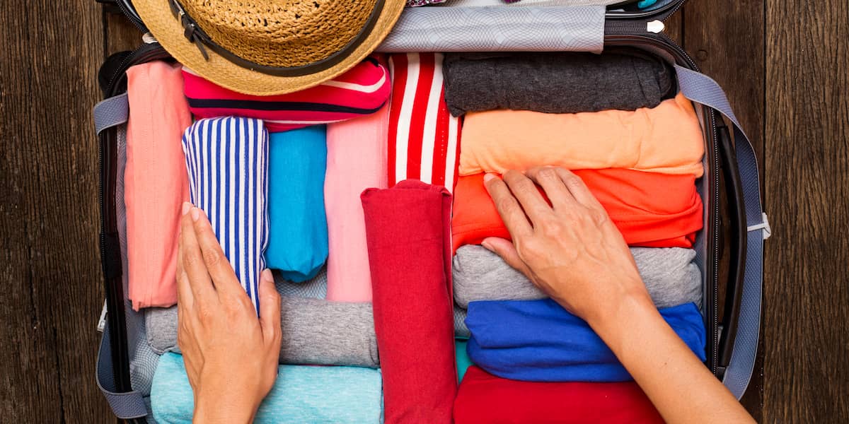 Hands organizing rolled shirts in a suitcase as the best way to pack clothes for moving, using space-saving and wrinkle-prevention methods.
