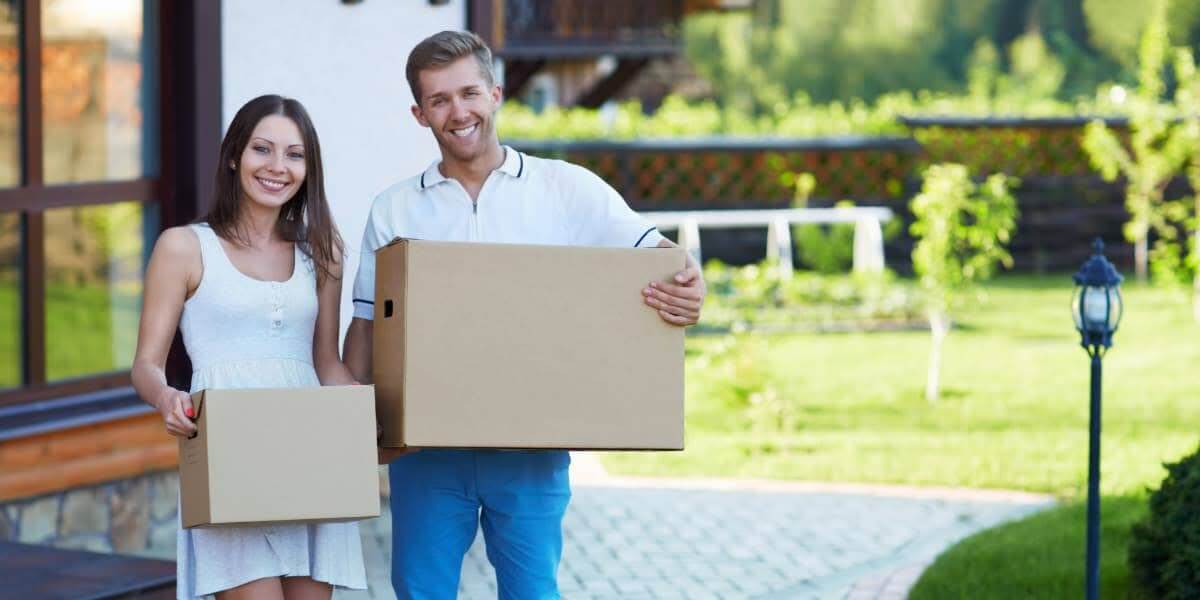 Couple carrying boxes outside a home during a move, illustrating summer moving tips in South Florida heat